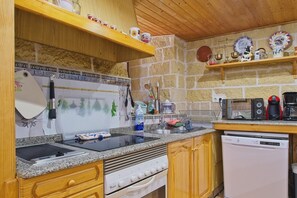 Una cocina con encimeras de granito, estufa, lavavajillas, armarios de madera y diferentes utensilios y electrodomésticos.