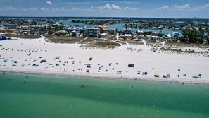 An aerial view of a beach with numerous umbrellas and people, a marina with boats, and buildings in the background. - 2BR 2Ba Treasure Island Luxury waterfront updated Condo., steps to beach access (Treasure Island)