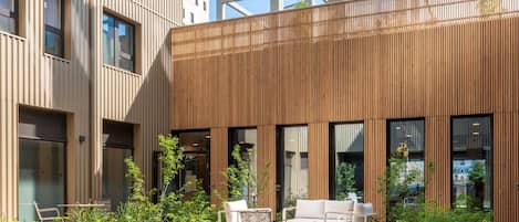 An outdoor seating area with tables and chairs, surrounded by plants and a wooden fence.