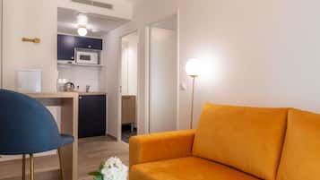 Een kleine leefruimte met een kitchenette, een bank, een stoel en een vloerlamp.