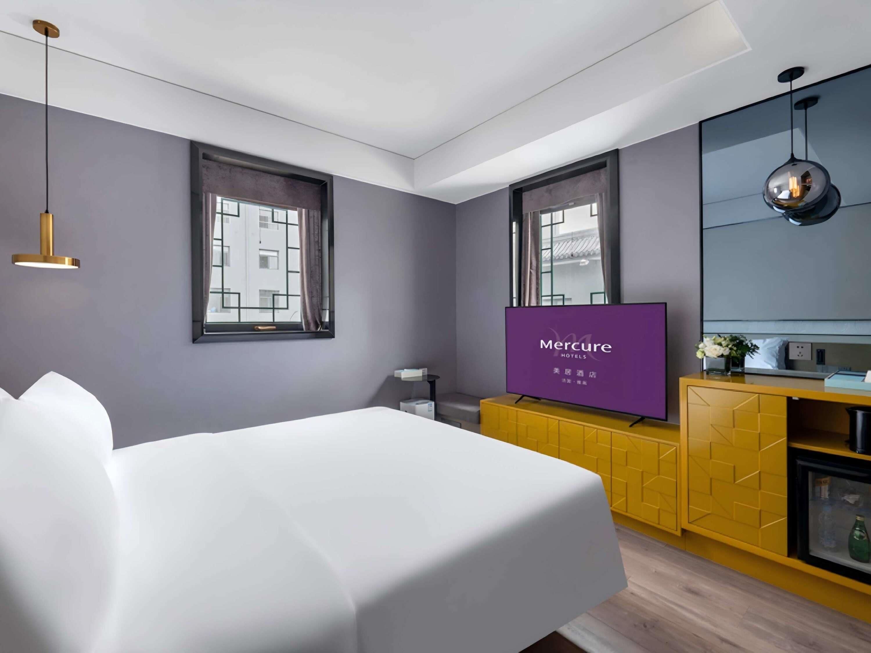 Une chambre d’hôtel avec un lit, une télévision, une armoire jaune et une fenêtre.