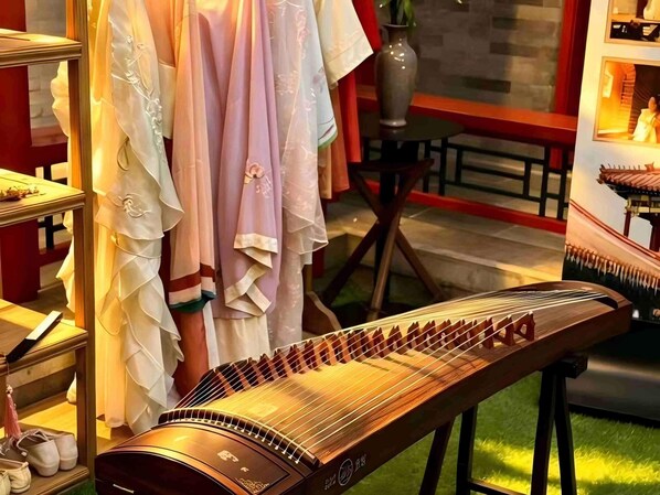 Un instrumento de cuerda tradicional, posiblemente un guzheng, en una habitación con suelo de madera y un jarrón sobre una mesa.