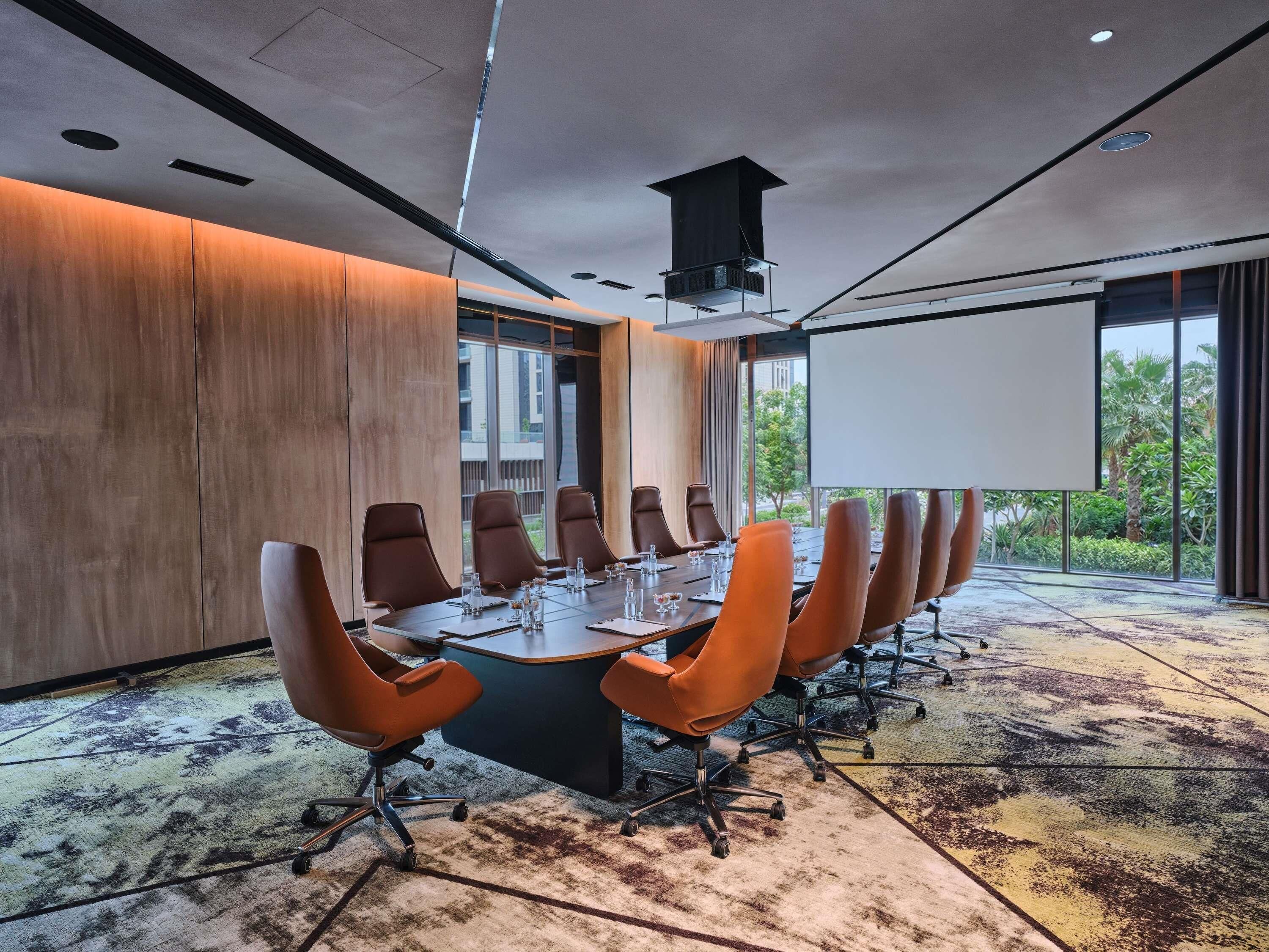 A conference room with a long table, multiple chairs, a projector screen, and large windows.