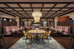 A restaurant with a central round table surrounded by chairs, booths on the sides, and a patterned floor. - Raffles The Red Sea (Umluj)