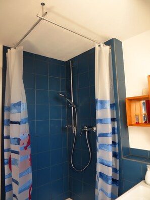 Une douche avec un rideau, un pommeau de douche à main et un robinet fixé au mur.
