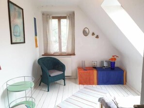 Une petite pièce lumineuse, avec une fenêtre, une chaise, une table ornée d’un vase et un radiateur.