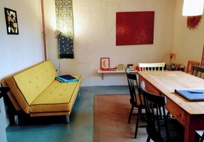 Une pièce avec un canapé jaune, une table à manger en bois avec des chaises, un mur d’accent rouge et une petite étagère avec quelques objets.