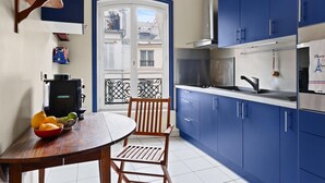 A compact kitchen with blue cabinets, a stove, and a dining area with a table and chairs. - Stylish 1BR in the Heart of Paris by Louvre (Paris)