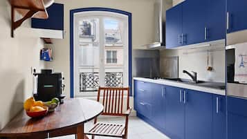 Een compacte keuken met blauwe kastjes, een fornuis en een eethoek met een tafel en stoelen.