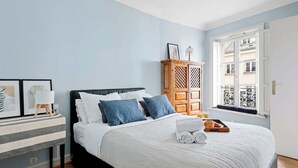 A bedroom with a bed, a wooden cabinet, a window with a view, and a bedside table with a lamp. - Stylish 1BR in the Heart of Paris by Louvre (Paris)
