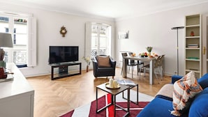A living room with a TV, a dining area, a sofa, and a bookshelf. - Stylish 1BR in the Heart of Paris by Louvre (Paris)