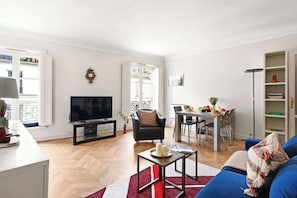 A living room with a TV, a dining area, a sofa, and a bookshelf. - Stylish 1BR in the Heart of Paris by Louvre (Paris)