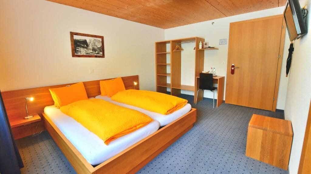 A bedroom with a wooden bed, a wardrobe, a desk, and a television.