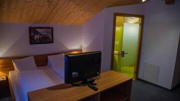 Un dormitorio con cama, un televisor sobre una mesa de madera, un cuadro en la pared y una puerta iluminada de verde.