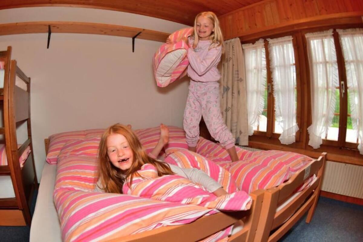 A bunk bed room with striped bedding, wooden walls, and a window with curtains.