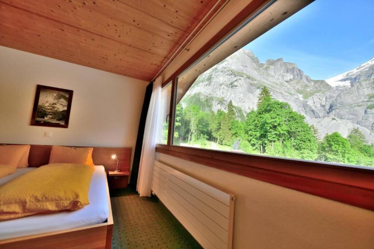 A room with a bed, a nightstand, a window with a mountain view, and a framed picture on the wall.