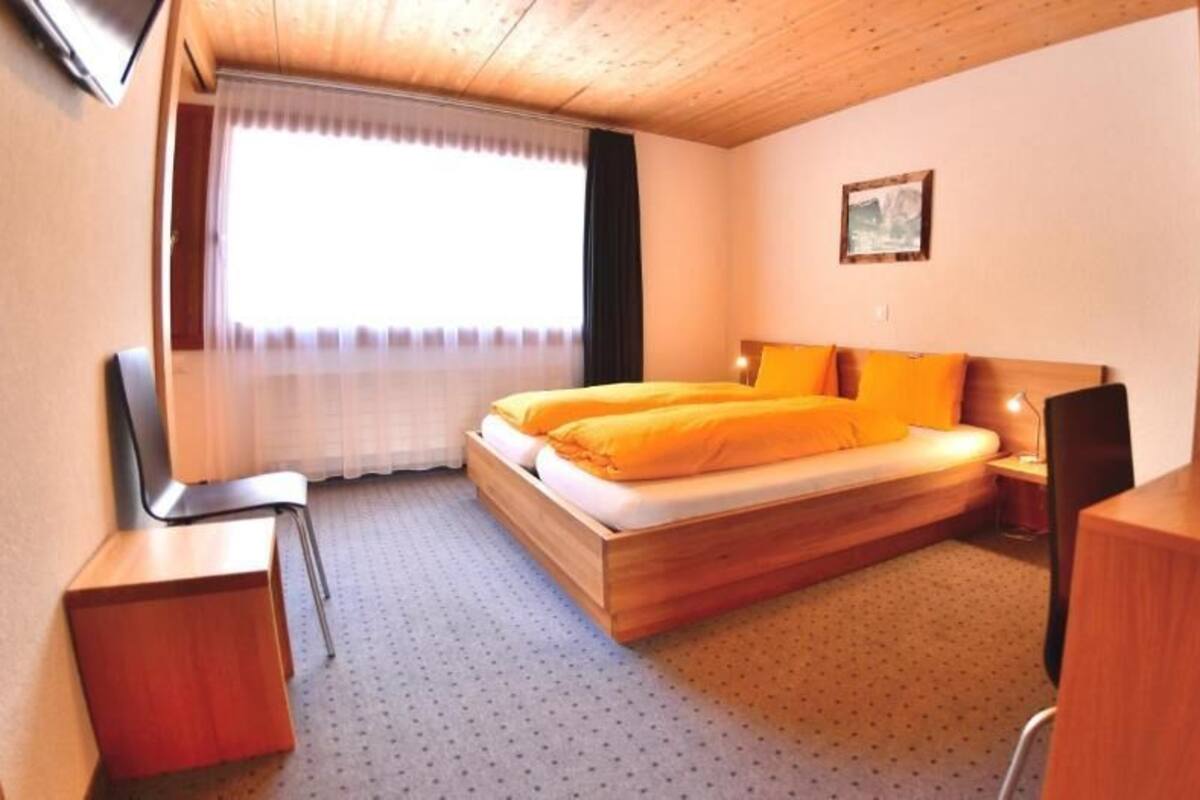 A room with a bed, a desk, a chair, a window with curtains, and a painting on the wall.