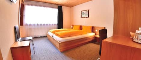 A room with a bed, a desk, a chair, a window with curtains, and a painting on the wall.