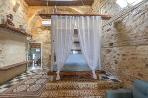 Una habitación con una cama, piso a cuadros, un banco y vista a través de un arco.
