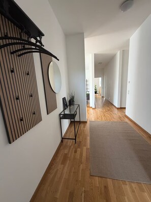 Ein geräumiger Flur mit Holzboden, einem schwarzen Metallkonsole und einem runden Spiegel sowie einer dekorativen Wandverkleidung.