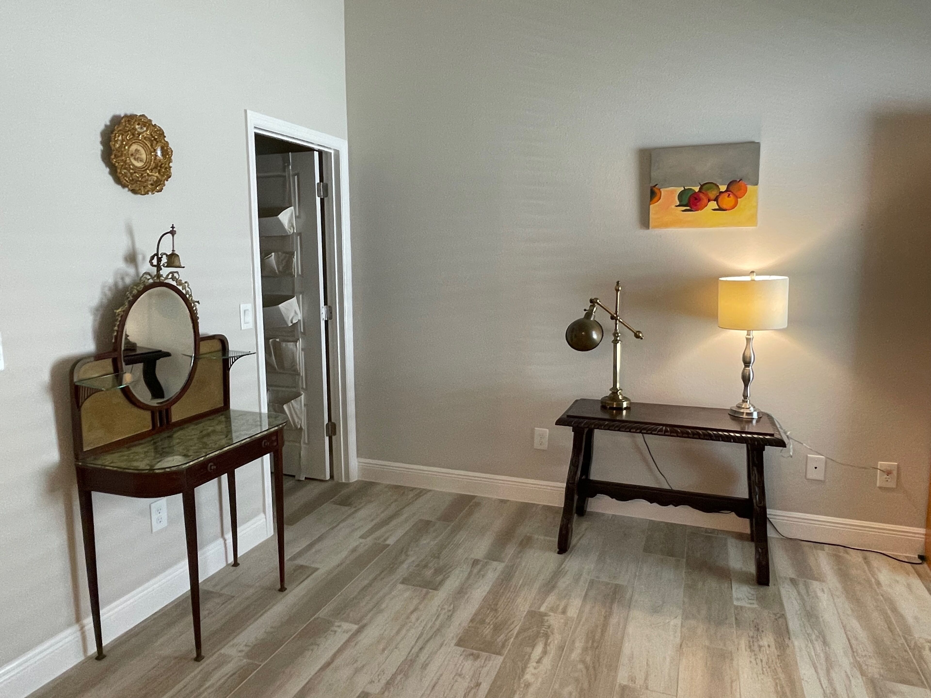 Ein Zimmer mit Holzboden, einem Spiegel mit Glasplatte, einem Schreibtisch mit Lampe und einer Tür zu einem Kleiderschrank.