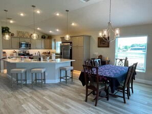 A modern kitchen with a central island, dining area with a table and chairs, and a large window with a view.
