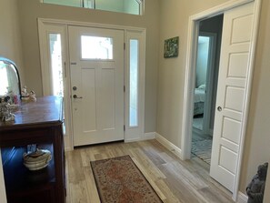 A hallway with a wooden floor, a rug, a dresser with a mirror, and a door leading to a bedroom.