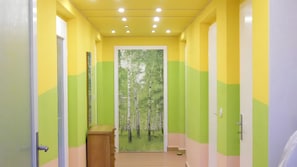 Ein Korridor mit grünen und gelben Wänden, einem Holzkabinett und einer Tür, die zu einem Zimmer mit Blick auf einen Wald führt.
