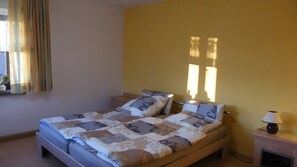 A single bed with a patterned bedspread and pillows, a bedside table with a lamp, and a window with curtains.