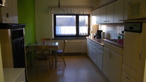 A compact kitchen with a dining table, chairs, a window with curtains, and basic appliances.