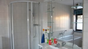 Ein modernes Badezimmer mit einer gläsernen Duschkabine, einem weißen Waschbecken und einem großen Spiegel.