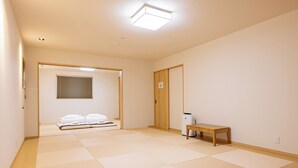 Een kamer met tatami vloerbedekking, een houten bank, een witte verwarming en een deur naar een andere kamer.