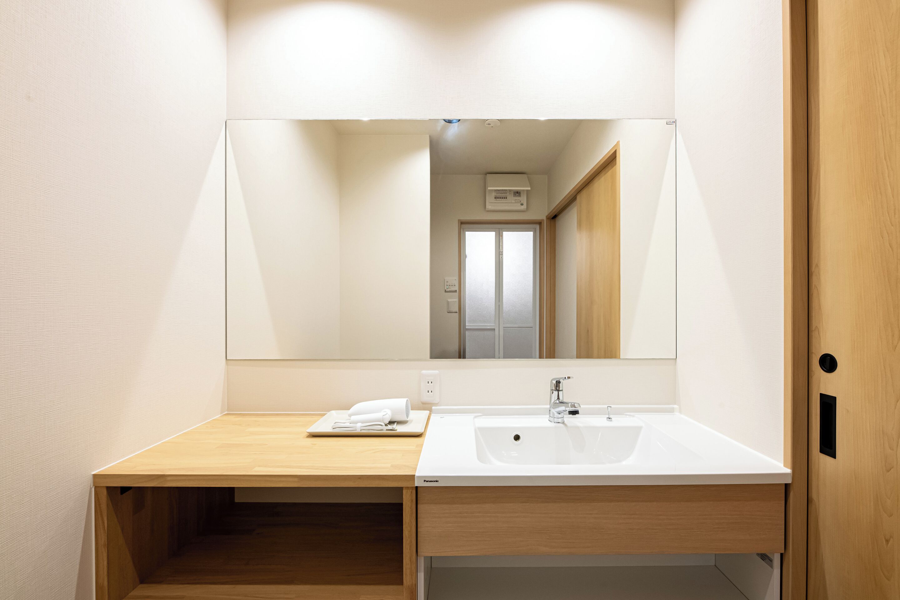 A modern bathroom with a wooden vanity, a white sink, and a large mirror.