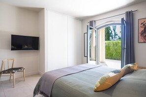 Ein Schlafzimmer mit Bett, Sessel, Fernseher und Blick auf Grünflächen.