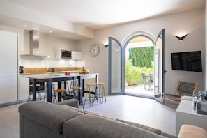 Eine moderne Küche mit Kochinsel, Essbereich inklusive Sofa und Stühlen sowie ein großes Schiebeglastür zum Patio mit Gartenmöbeln.