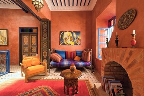 A Moroccan-style room with a sofa, a small table, a fireplace, and a painting on the wall. - Elegant Refuge in Medina with Ocean View (Essaouira)