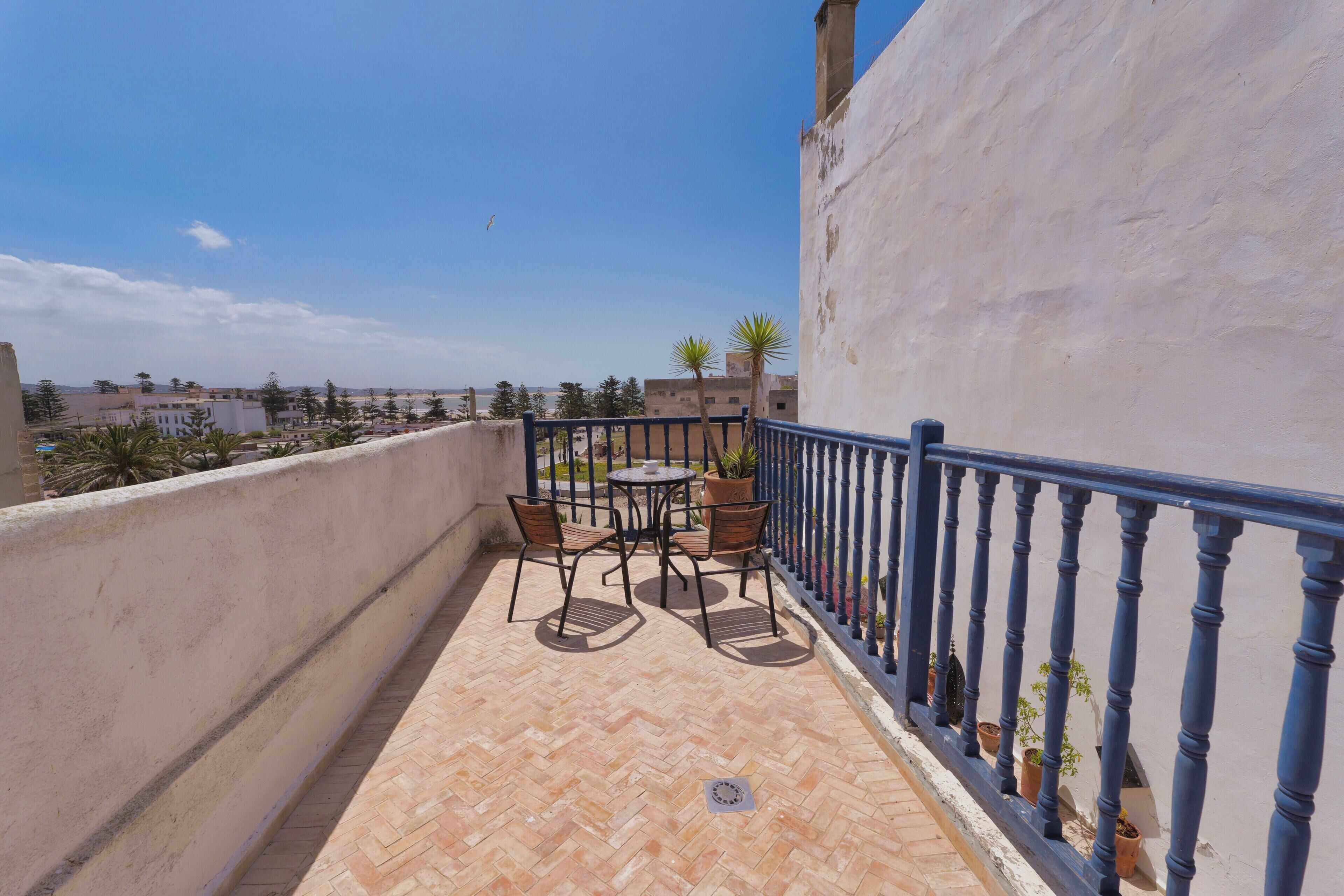 A balcony with a tiled floor, a table with chairs, and potted plants.