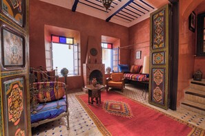 A traditional interior with a patterned rug, a sofa, a bed with colorful bedding, and a fireplace. - Elegant Refuge in Medina with Ocean View (Essaouira)