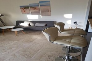 Una sala de estar moderna con un sofá gris, dos mesas redondas y dos sillas con respaldo alto.