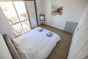 Ein Schlafzimmer mit Bett, Heizkörper, Fenster und Balkon.