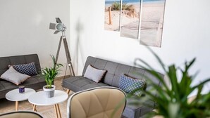 Ein modernes Wohnzimmer mit einem grauen Sofa, zwei weißen runden Tischen, einer Stehlampe und einem Blumentopf.