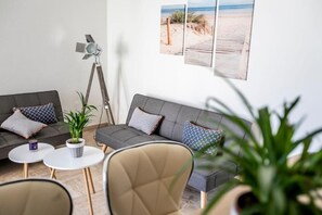 Ein modernes Wohnzimmer mit einem grauen Sofa, zwei weißen runden Tischen, einer Stehlampe und einem Blumentopf.