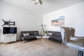 Ein modernes Wohnzimmer mit einer Couch, zwei runden Tischen, einem Fernseher und einem Deckenventilator.