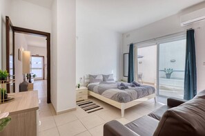 Ein modernes Schlafzimmer mit Bett, Nachttischen, einem Schreibtisch und einem Balkon mit Vorhängen.