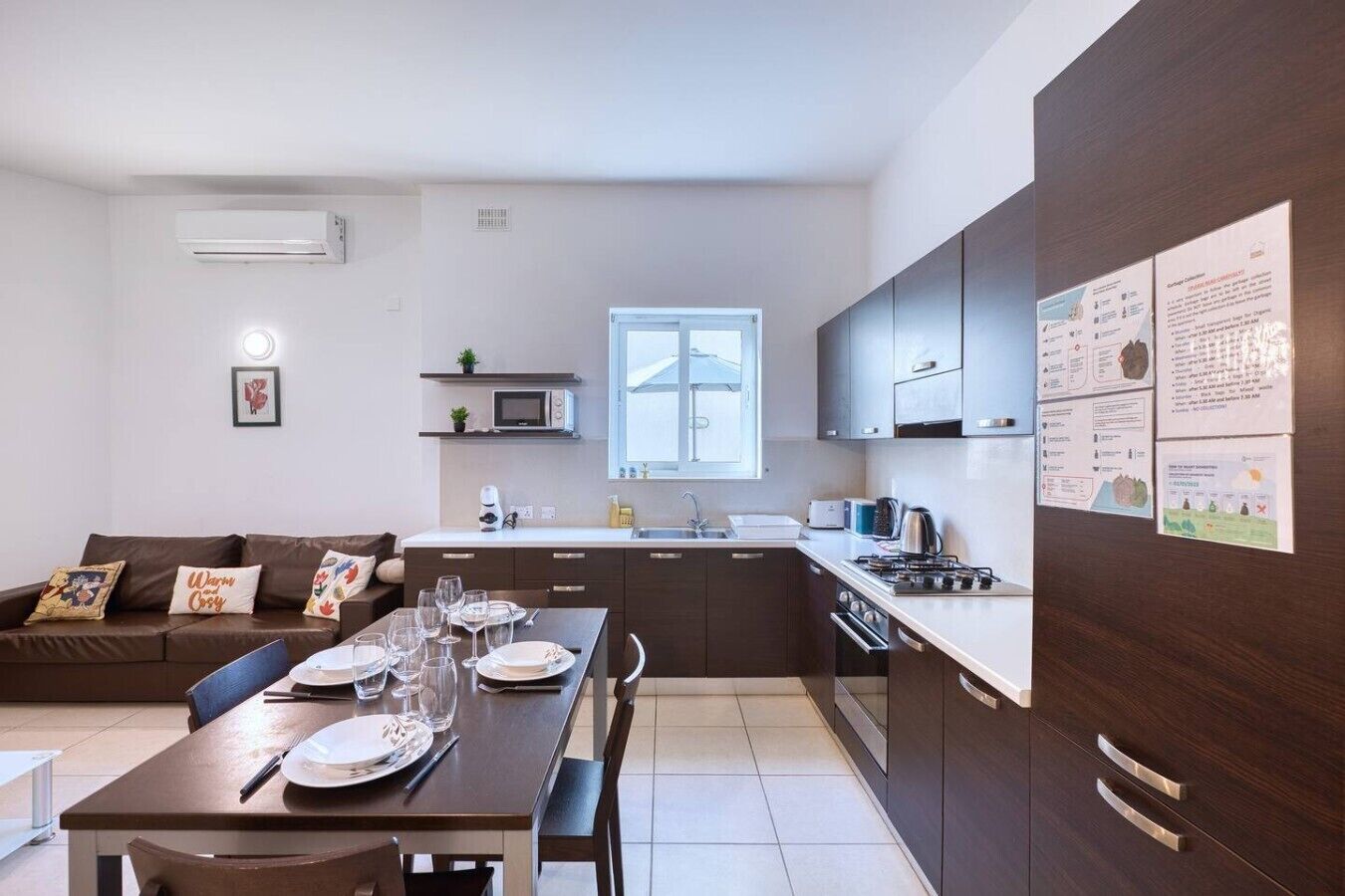 A modern kitchen with dark cabinets, a dining table set for four, and a window above the sink.