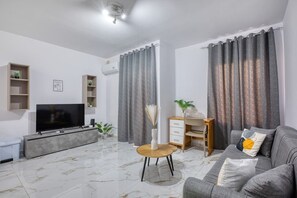Ein modernes Wohnzimmer mit Flachbildfernseher, einem Holztisch, einem grauen Sofa und einem Marmorboden.