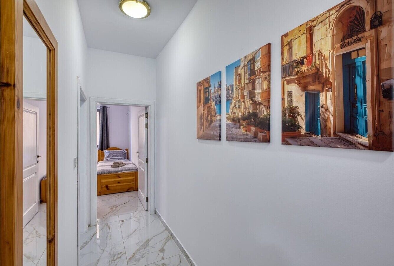 A hallway with a bed, white walls, and three paintings.