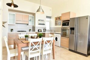A modern kitchen with a dining area, stainless steel appliances, and a washing machine. - Luxury Maltese Penthouse with Breathtaking views (Il-Mellieħa)