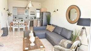 Una sala de estar moderna con un sofá gris, una mesa de centro de madera y un comedor con sillas blancas.