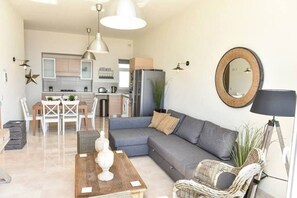 A modern living room with a grey sofa, a wooden coffee table, and a dining area with white chairs. - Luxury Maltese Penthouse with Breathtaking views (Il-Mellieħa)